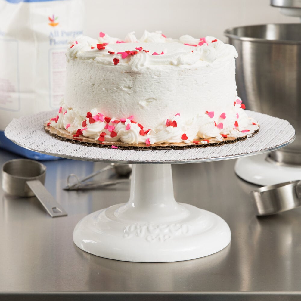 White frosted cake with red and pink decorations on a Ateco white cast iron base cake stand in a kitchen setting.