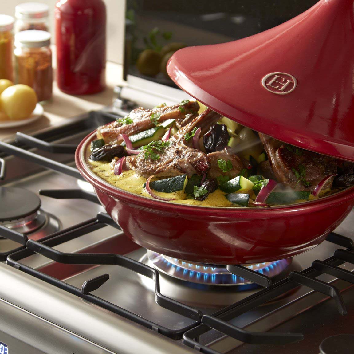 Red Dutch oven tagine on a stovetop with food inside, Emile Henry brand logo visible