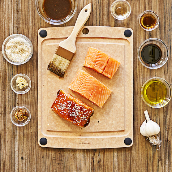 Salmon fillets on a wooden composite Epicurean all-in-one cutting board with various seasonings and oils on a wooden surface.
