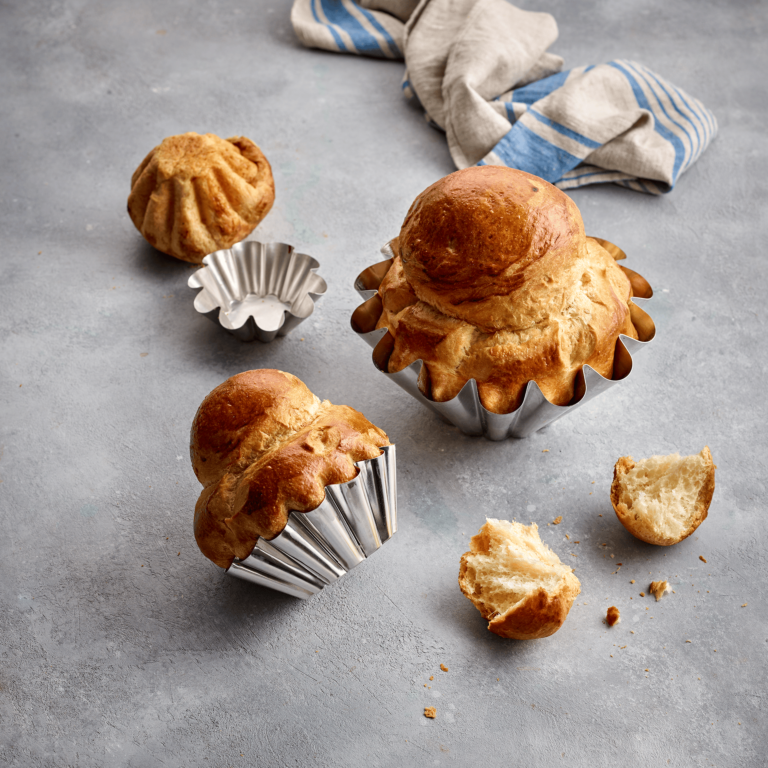 Brioche in metal Gobel moulds on a gray surface with a striped cloth in the background.