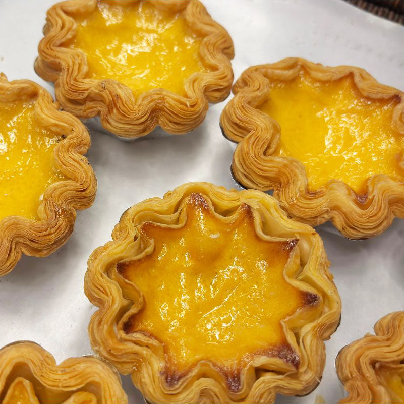 Egg tarts with wavy crust on a white surface