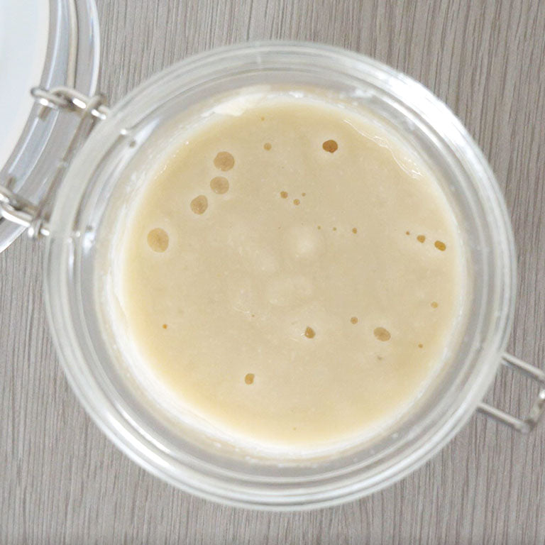 Glass jar with a creamy white Japanese bread starter on a wooden surface