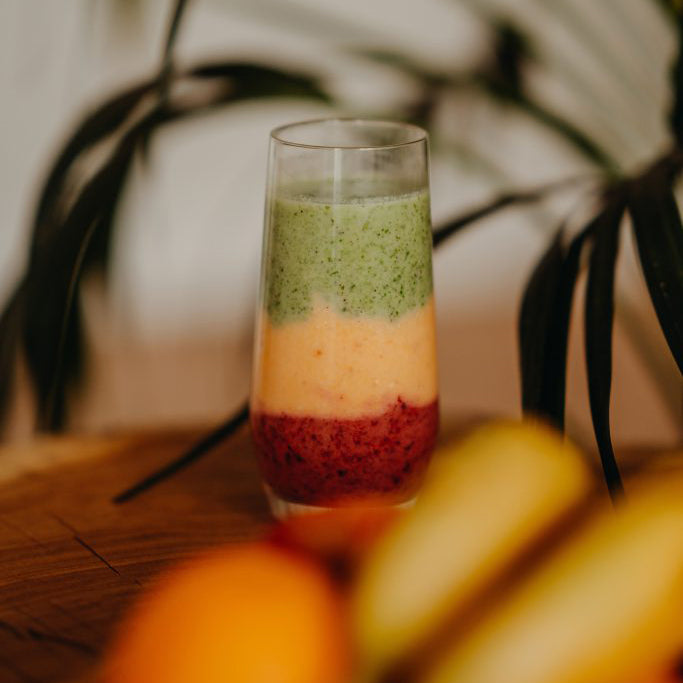 Layered smoothie in a glass with fruits on a wooden surface