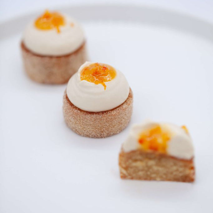 Three small dessert pastries with white cream and orange zest on a white background