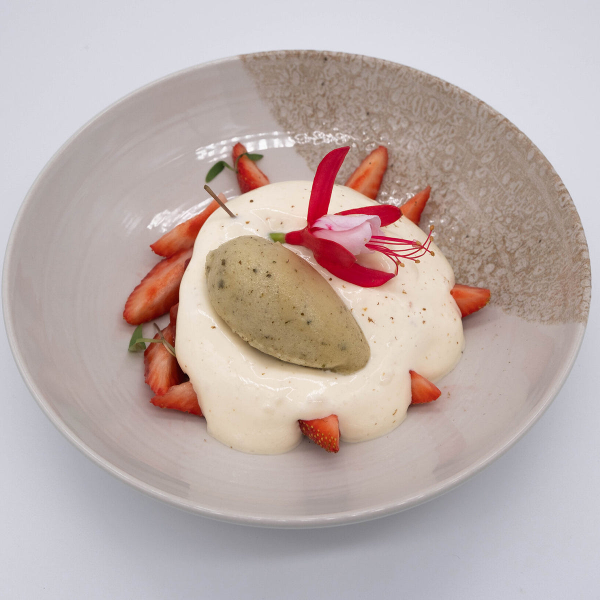 Dessert dish with meringue, strawberries, and a flower on a textured plate.