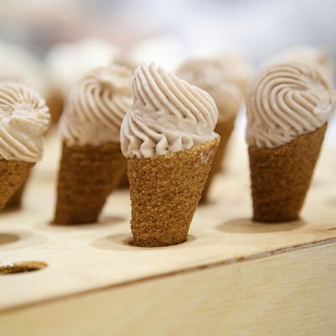 Small ice cream cones with beige frosting on a wooden surface
