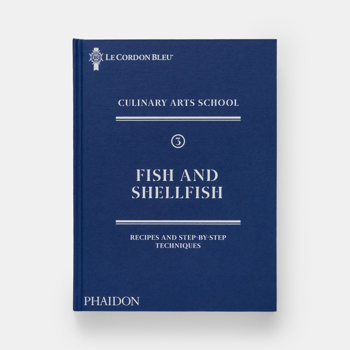 A hardcover book titled 'Fish and Shellfish' from Le Cordon Bleu Culinary Arts School, published by Phaidon. The book cover is a deep navy blue with white text and decorative lines, set against a light gray background.