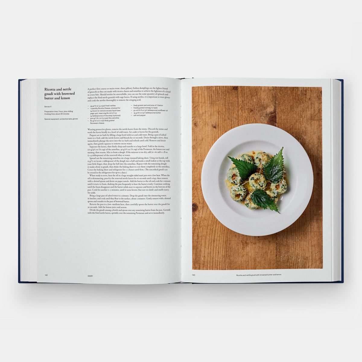 An open cookbook spread showing a recipe page on the left and a plated prepared dish on a wooden surface on the right, photographed against a light gray background.