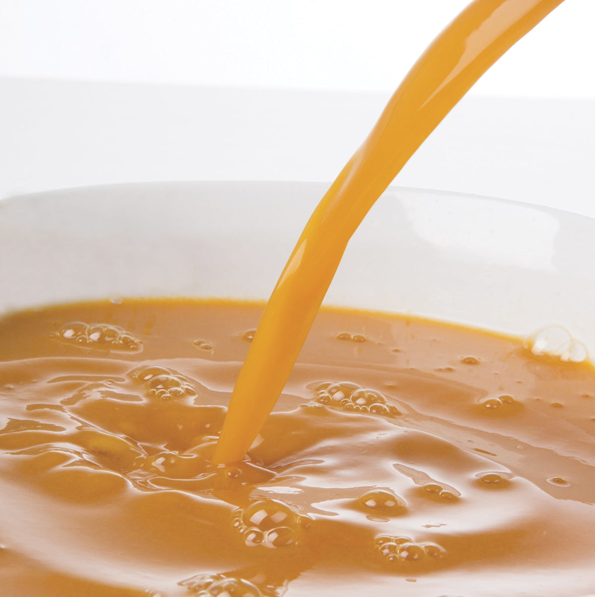 Pacific Fruit Golden Berry puree being poured into a white bowl on a light background
