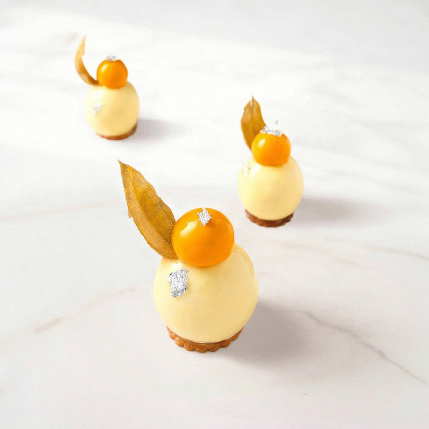 Delicate dessert with yellow sphere and golden berry topping on a white background