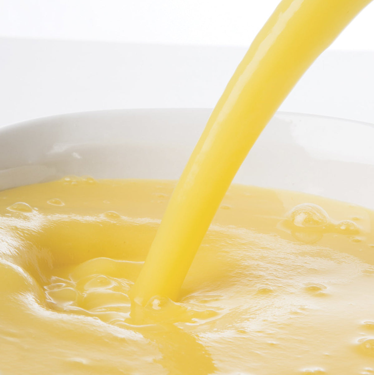 Yellow Pacific Fruit pineapple puree being poured into a white bowl on a white background
