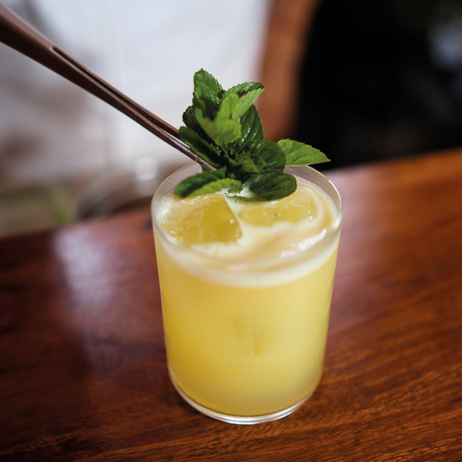 Glass of yellow lemon drink made with shelf stable puree, with a mint leaf on a wooden surface