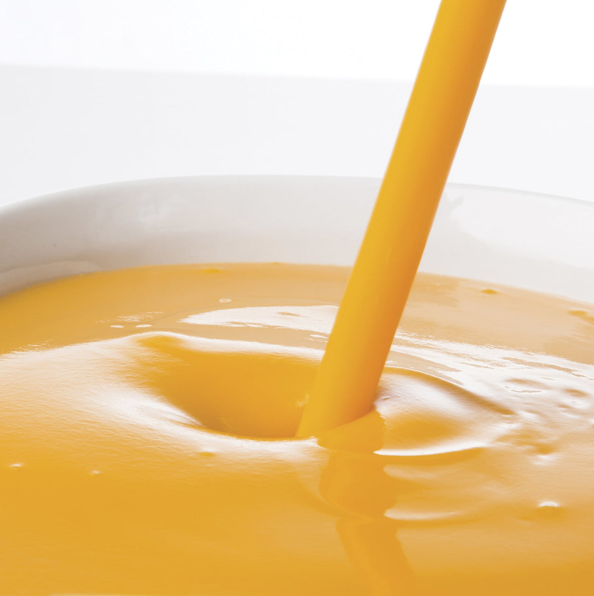 Pacific Fruit mango puree being poured into a glass with a straw on a white background