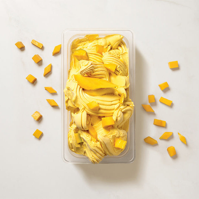 Container of mango ice cream using Pacific Fruit mango puree with scattered pieces on a light background