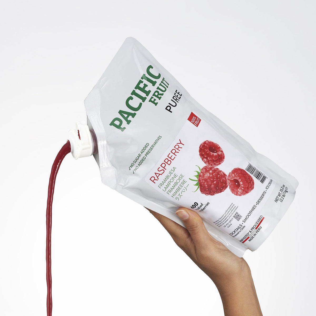 Hand holding a package of Pacific Fruit Puree Raspberry on a white background