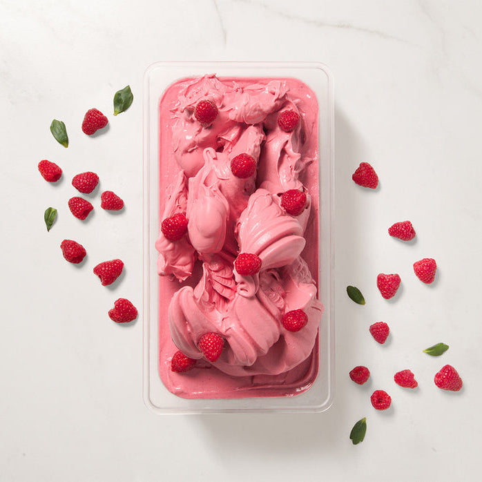 Pink raspberry ice cream made with Pacific Fruit shelf stable raspberry puree in a container on a white background