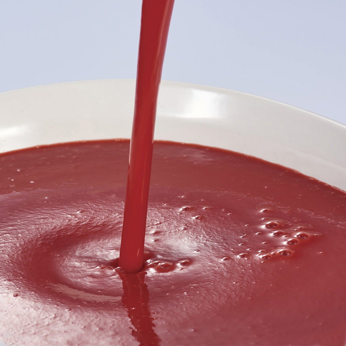 Red strawberry puree being poured into a white bowl against a light blue background