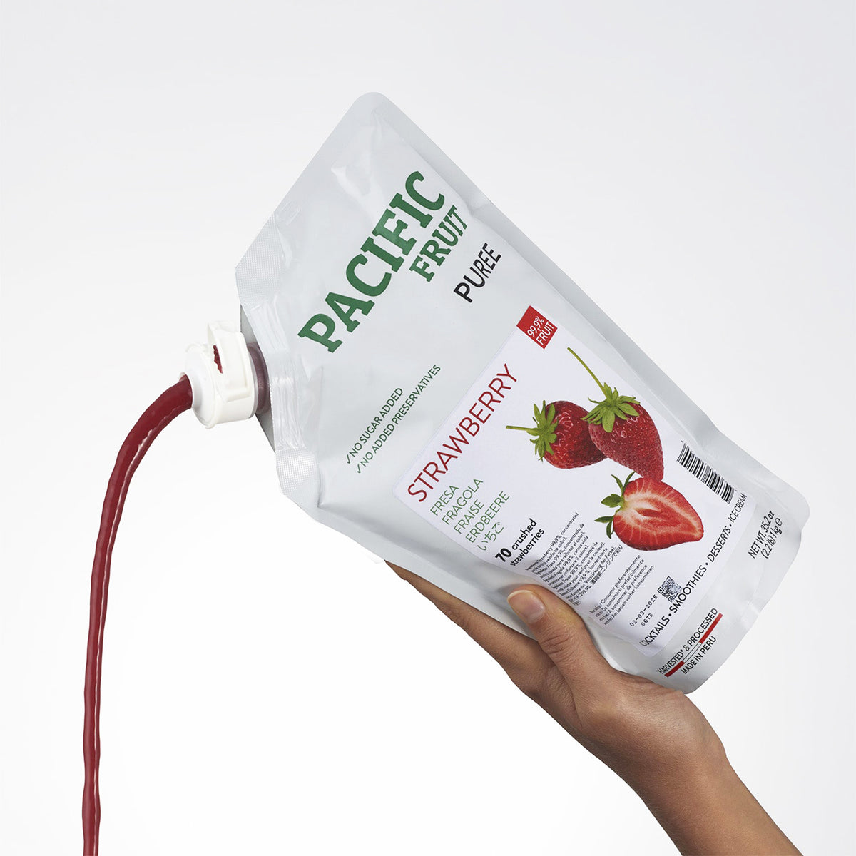 Hand holding a Pacific Fruit Puree strawberry pouch with a white background