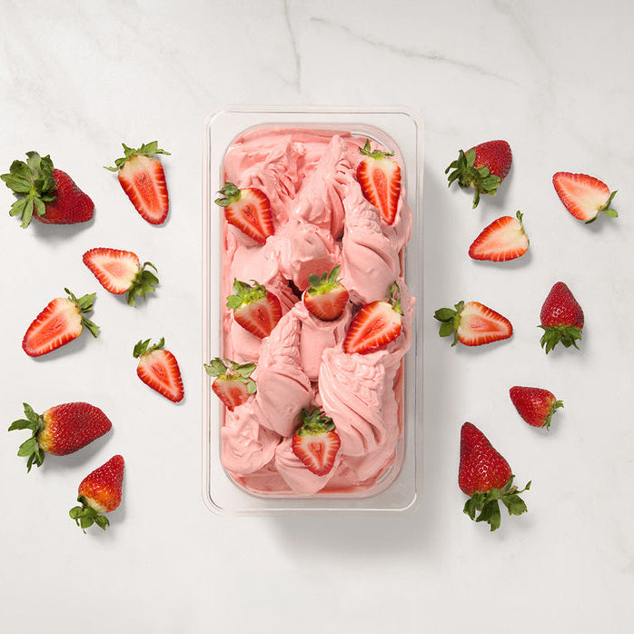 Strawberry ice cream made using puree in a container with sliced strawberries on a white background