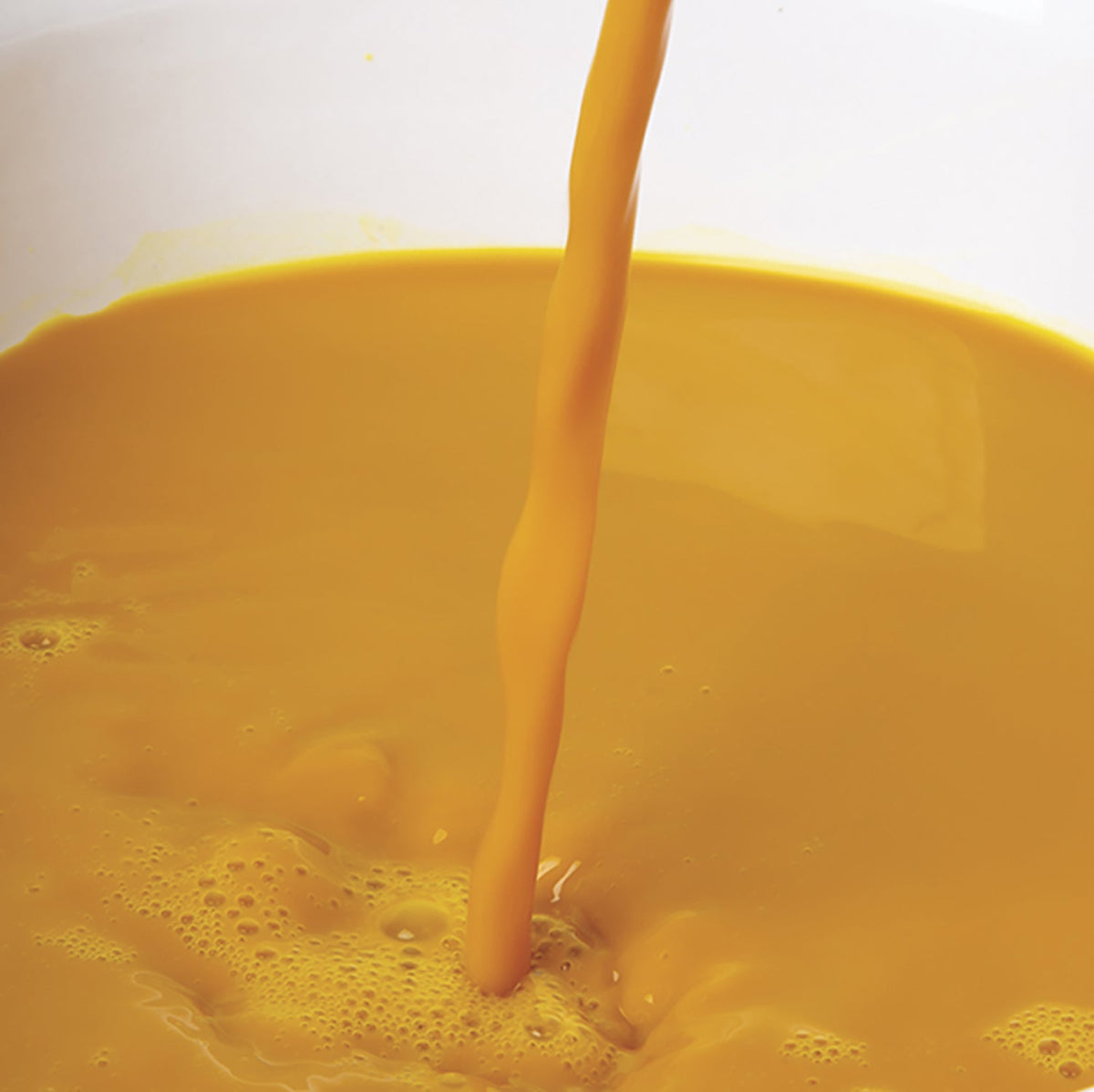 Yellow turmeric juice puree being poured into a container with a white background