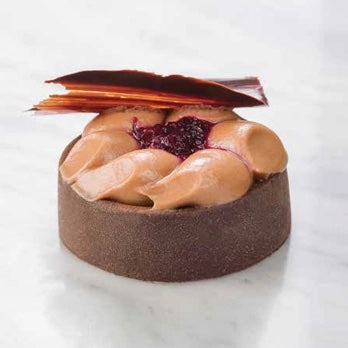 A gourmet chocolate mousse tart with light brown piped mousse, a dark berry compote, and a chocolate leaf garnish on a white marble background.