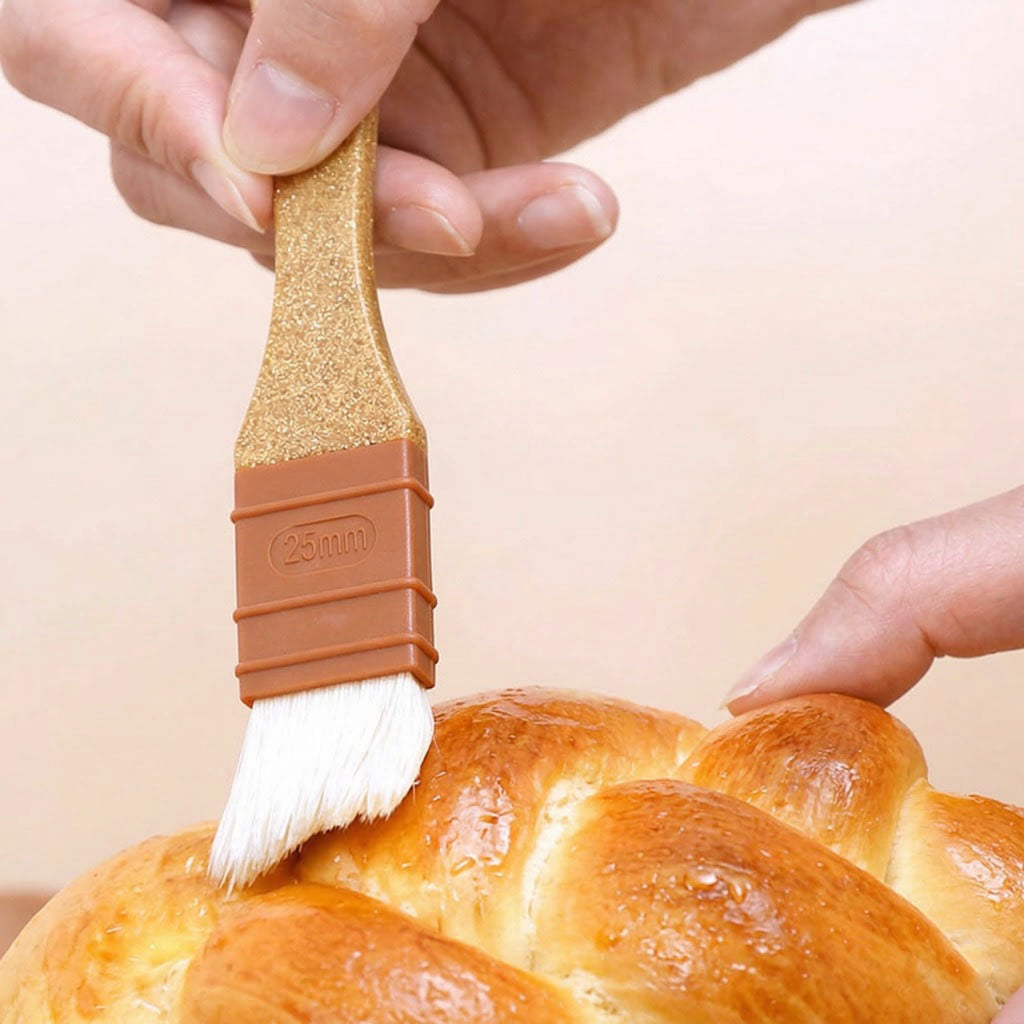 Person brushing a loaf of bread with a Sanneng eco handle pastry brush on a beige background