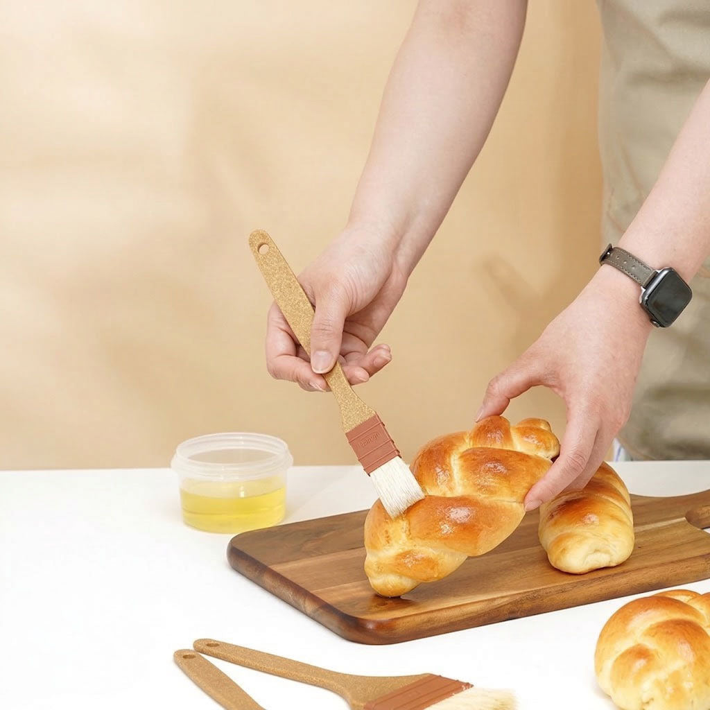 Person spreading butter on a loaf of bread with a Sanneng eco handle brush on a wooden board.