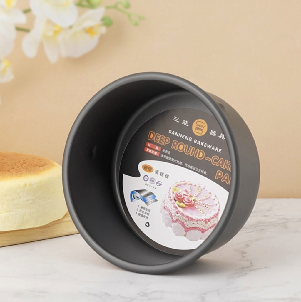 Black round Sanneng hard anodized deep round cake pan with a label on a light surface, next to a baked cake.
