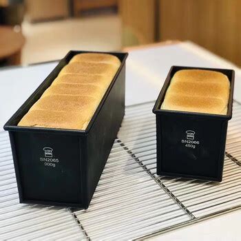 Two bread loaves in black Sanneng loaf pans on a cooling rack.