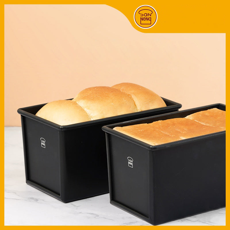 Two black loaf pans with bread inside on a marble surface, Sanneng logo at the top.
