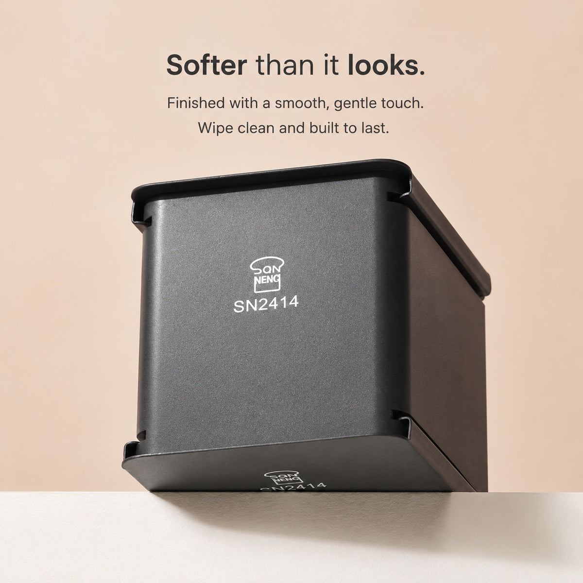 Sanneng matte black square wall-mounted dispenser or container with a lid, shown on a light beige background with promotional text above. The product has visible branding and model text on the front.
