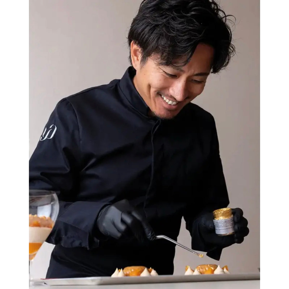 Chef Yusuke Aoki in black uniform preparing a dish with a focus on precision and care.