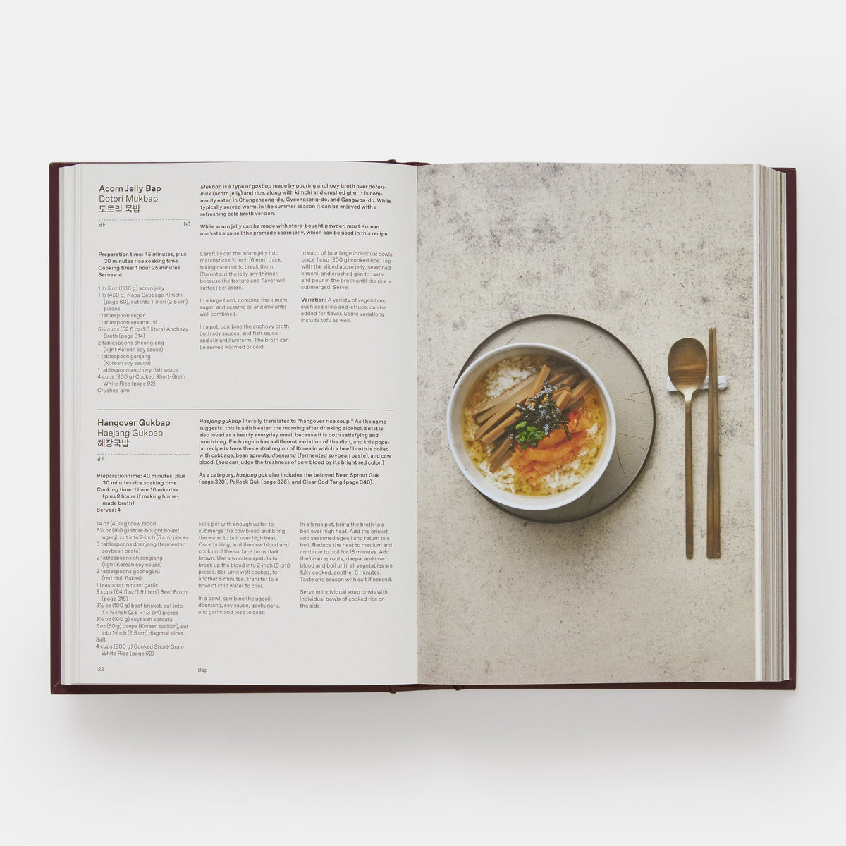 Open book showing a recipe with a bowl of soup and utensils on a concrete surface.
