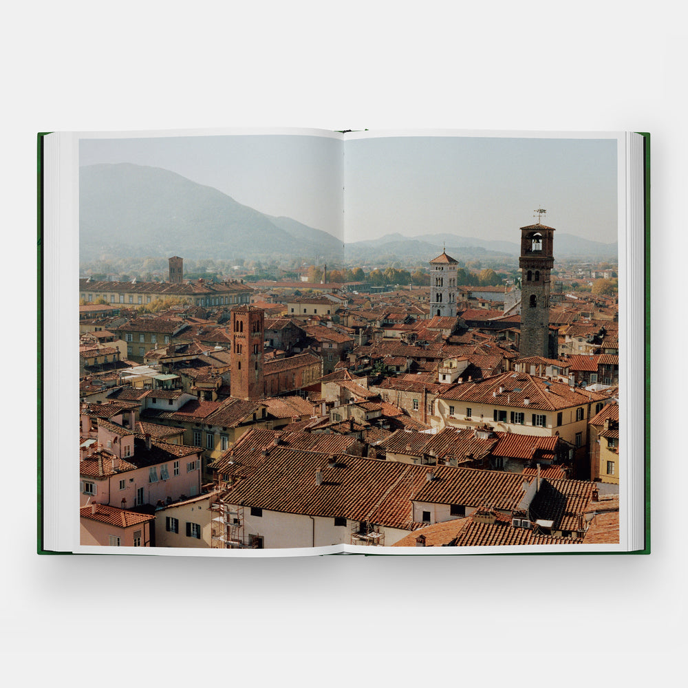 An open hardcover book showing a panoramic cityscape print with terracotta rooftops, church towers, and distant mountains under a hazy sky.
