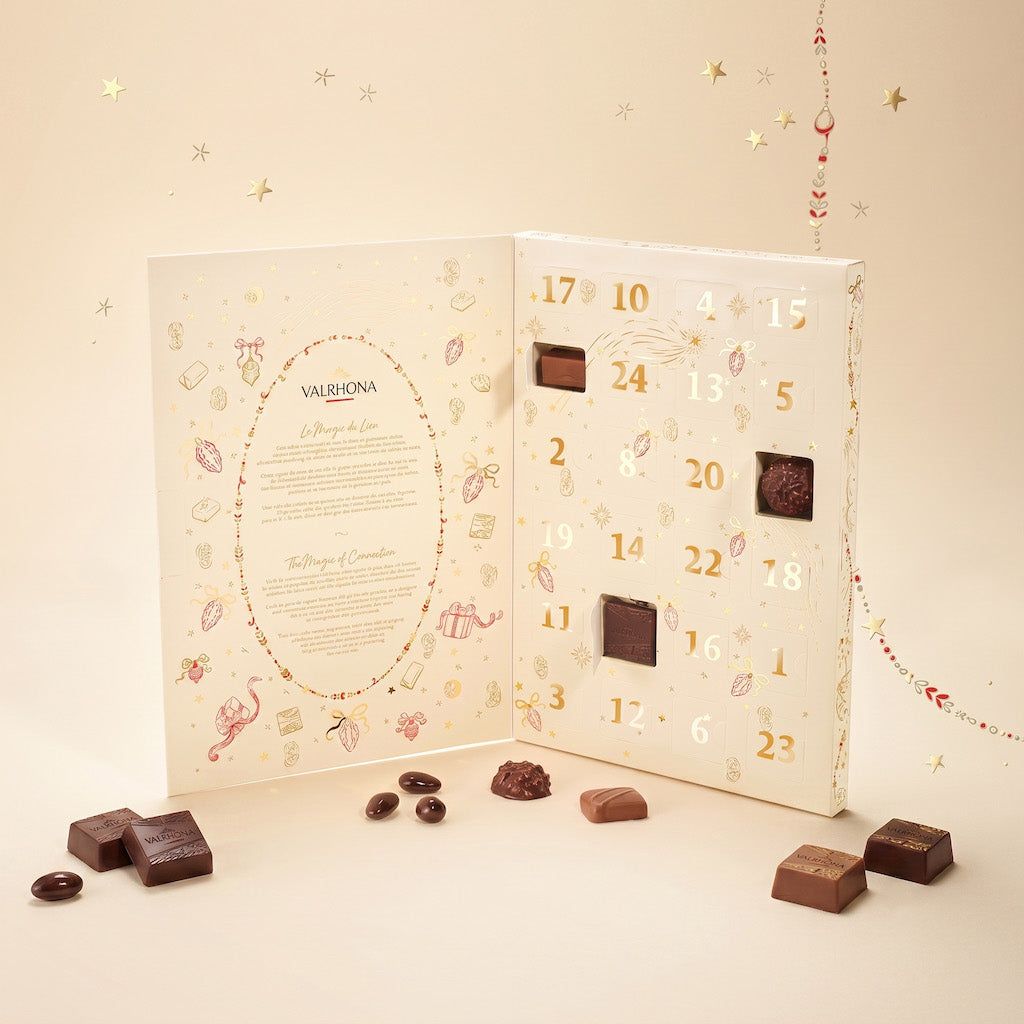 A Valrionna chocolate advent calendar shown open, with numbered compartments and several chocolate pieces placed in front on a warm cream background with small gold star decorations.