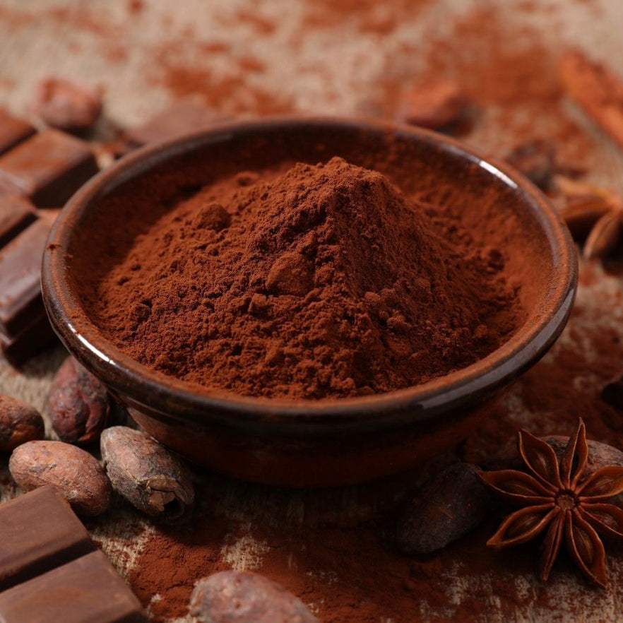 Callebaut cocoa powder extra brute in a wooden bowl surrounded by chocolate bars and cocoa beans on a brown background