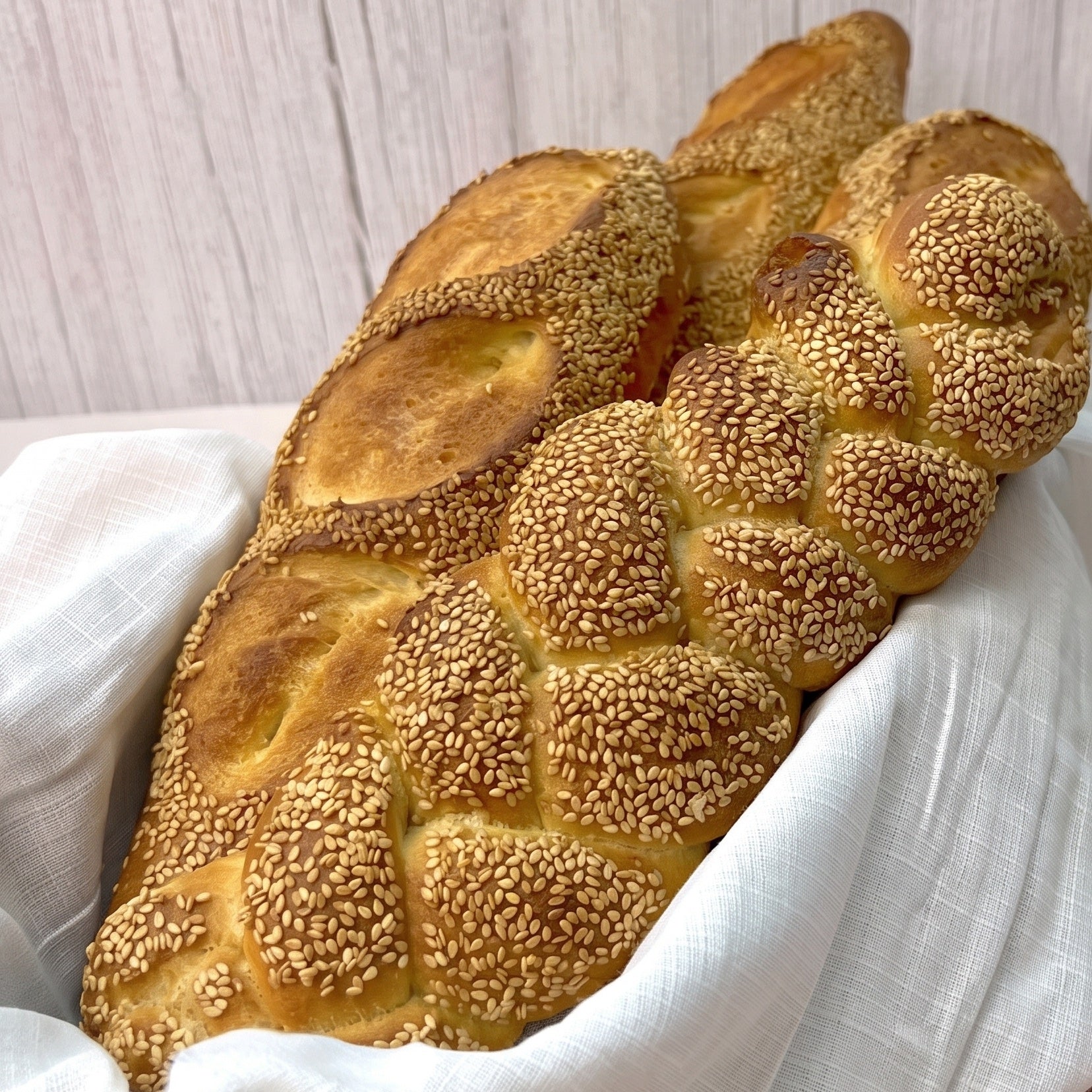 Two braided loaves of sesame seed bread, likely challah or matzo, resting on a white cloth.