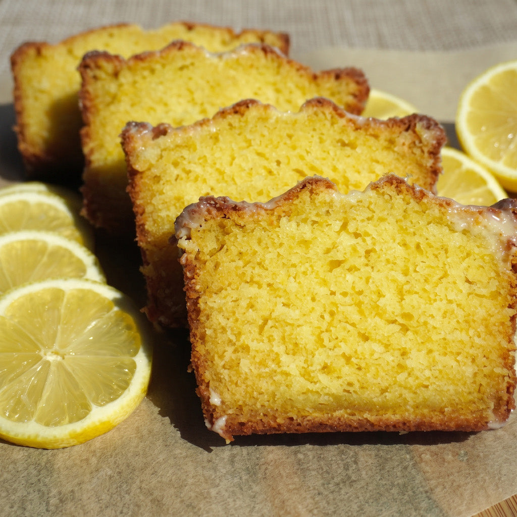 Slices of lemon gluten free cake arranged on parchment paper with lemon slices around them. The cake has a bright yellow interior and a golden-brown baked crust.