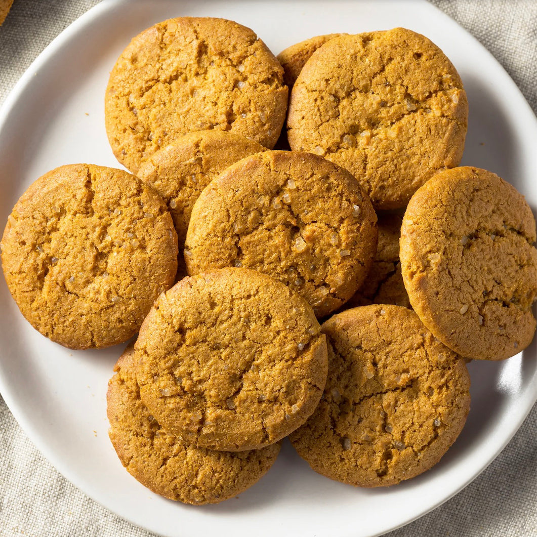 A pile of golden-brown pumpkin spice cookies stacked on a white ceramic plate, set against a neutral beige linen background.