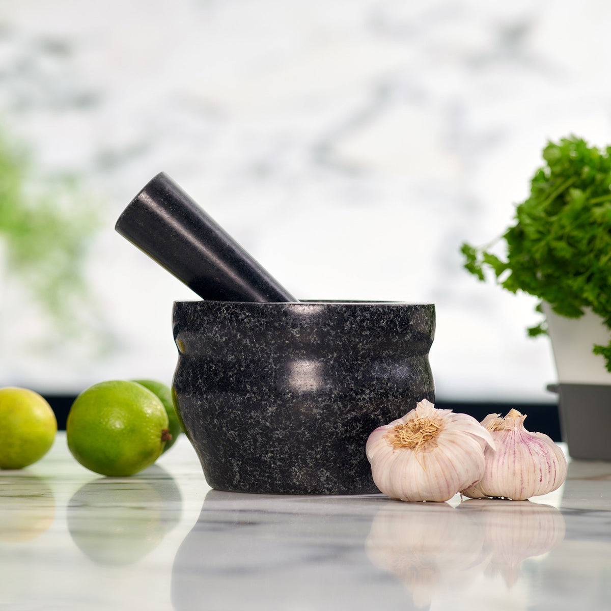 Black mortar and pestle with garlic and limes on a marble surface