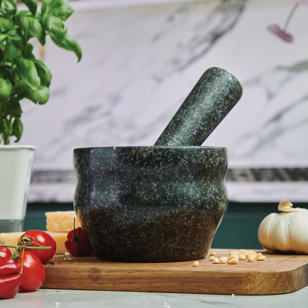 Mortar and pestle on a wooden cutting board with tomatoes and a plant in the background