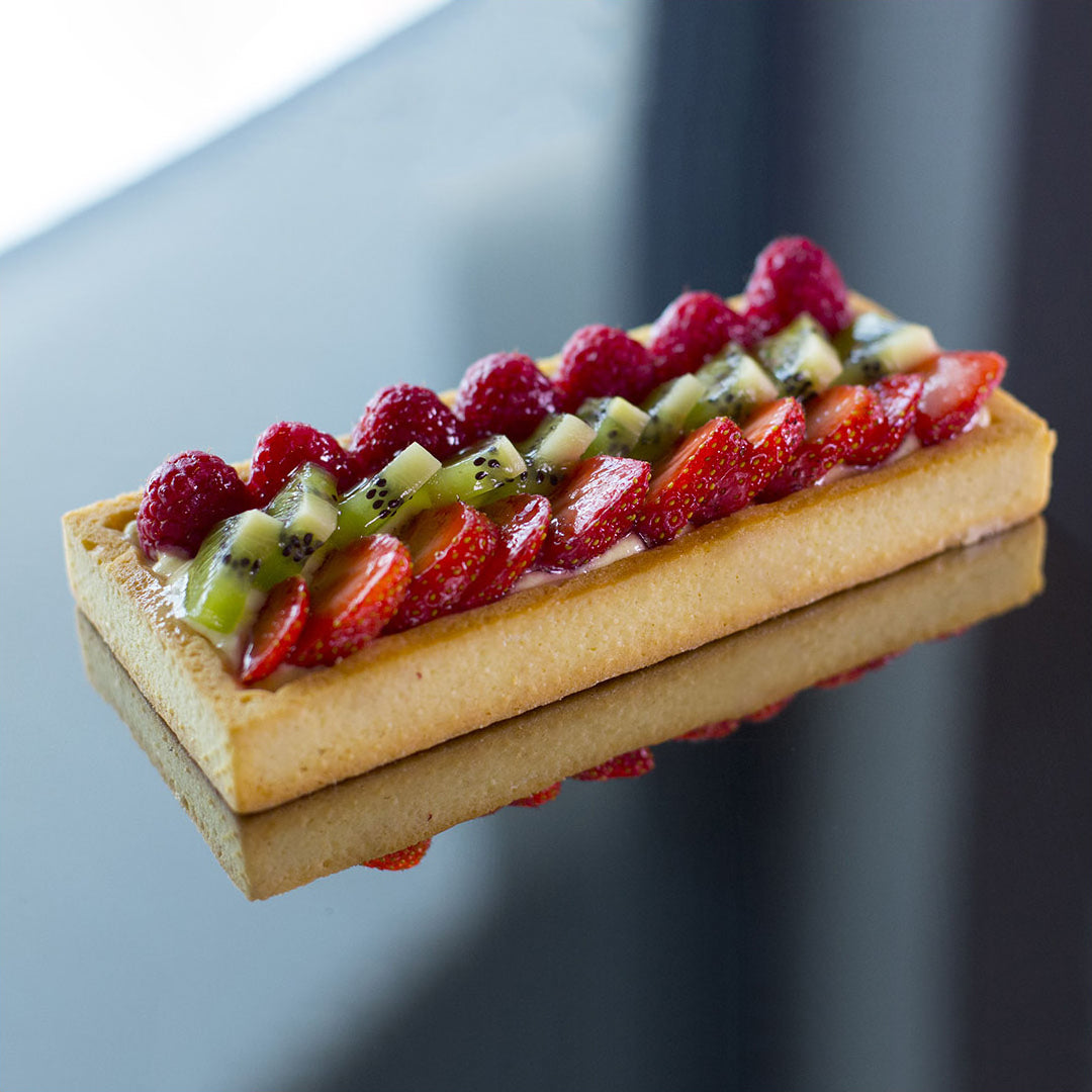 Fruit tart with strawberries, raspberries, and kiwis on a reflective surface