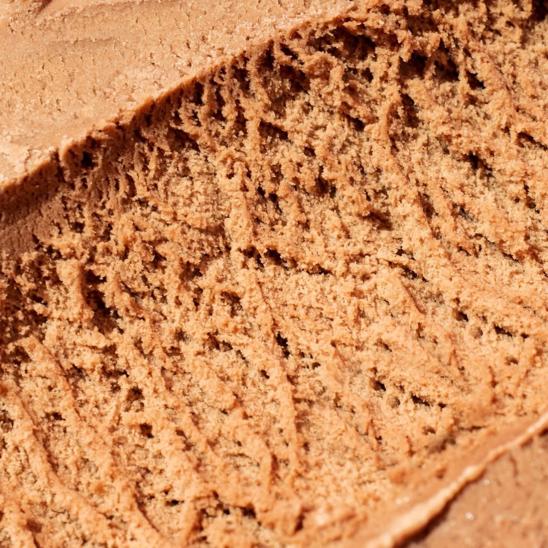 A close-up texture shot of a scoop of chocolate brown ice cream, showing its creamy, swirled consistency.