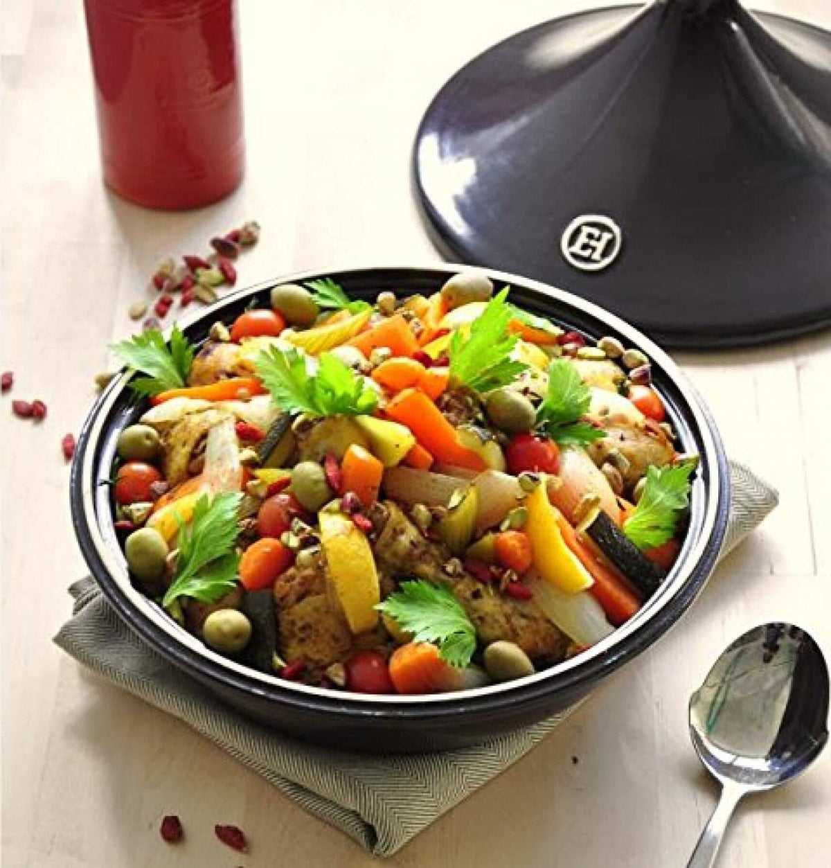 Colorful vegetable dish in a black bowl with a tagine lid on a white surface.