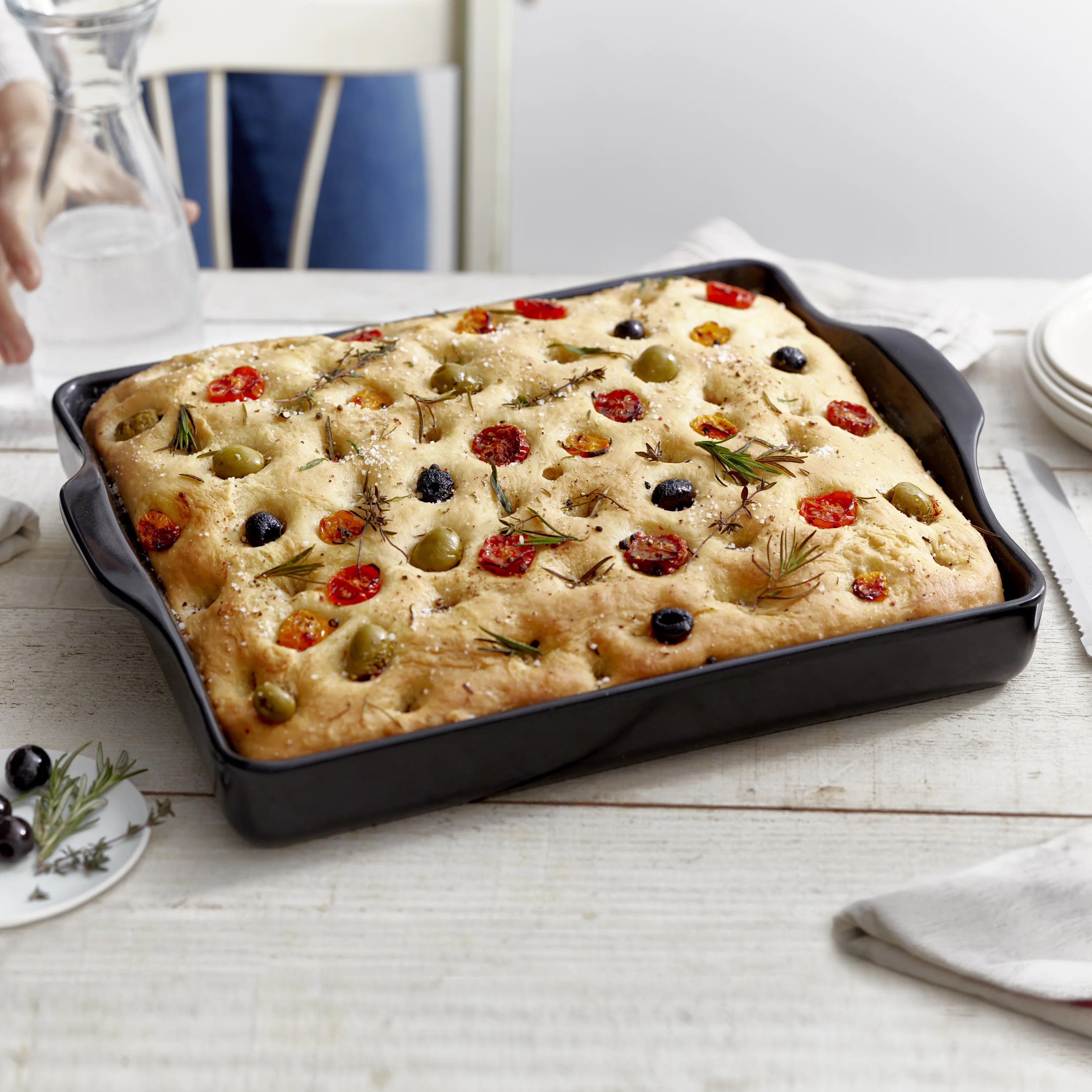 Baked focaccia bread with olives and tomatoes on a Emile Henry baking baker
