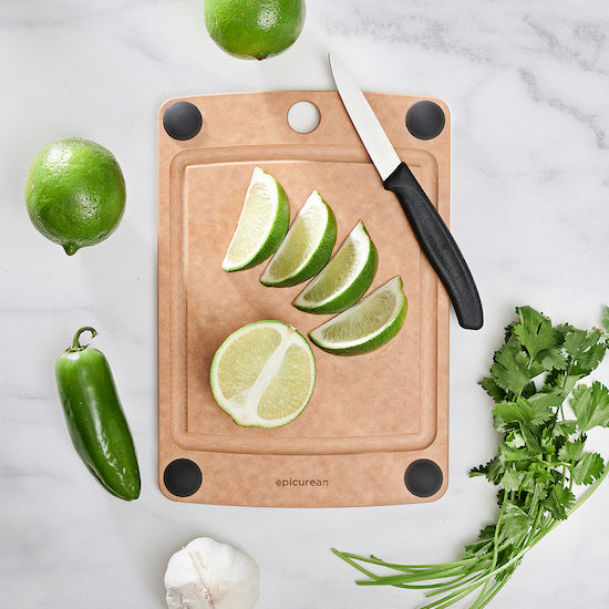 Epicurean all-in-one chopping board with sliced limes, a knife, and vegetables on a marble surface