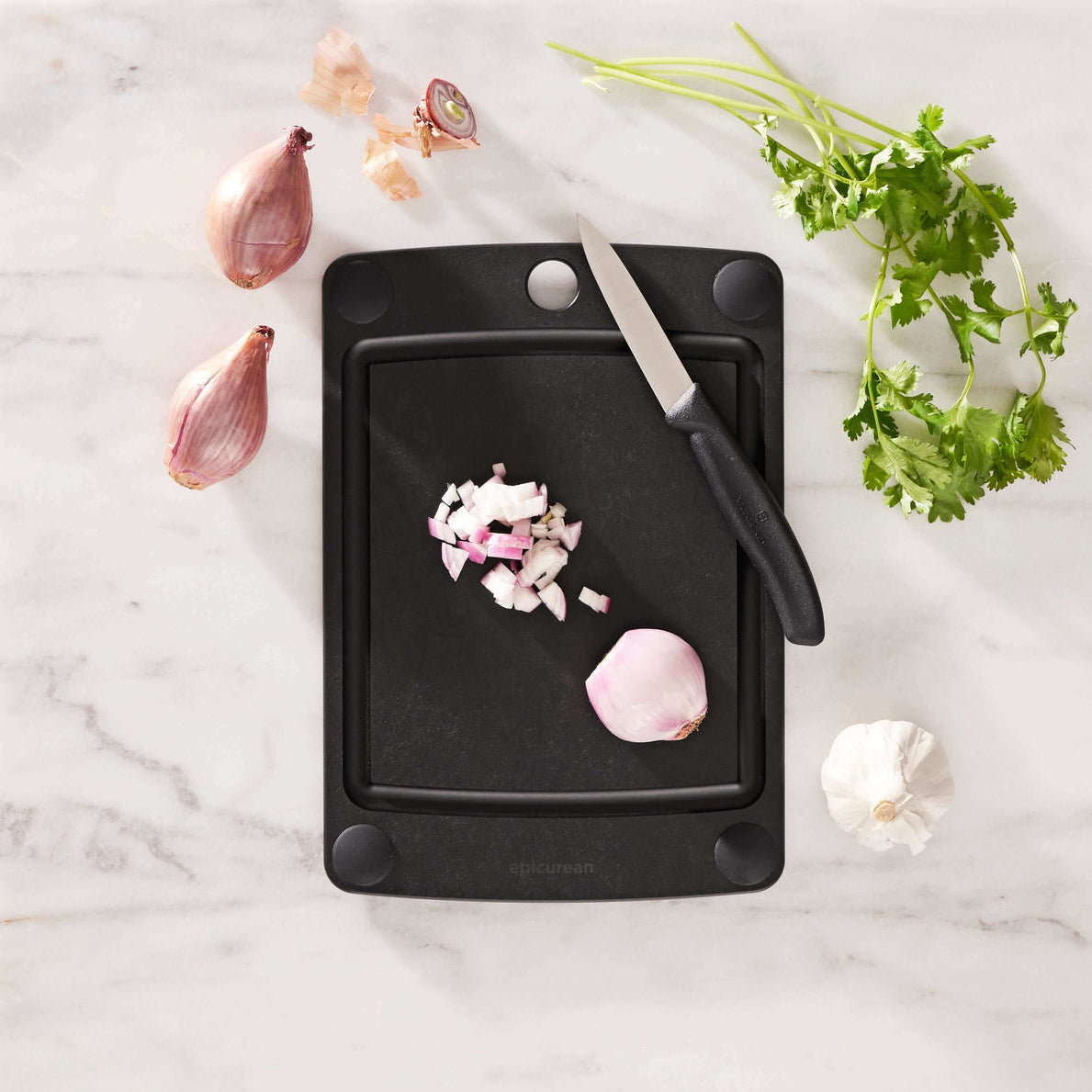Black Epicurean all-in-one series cutting board with chopped garlic and a knife on a marble surface