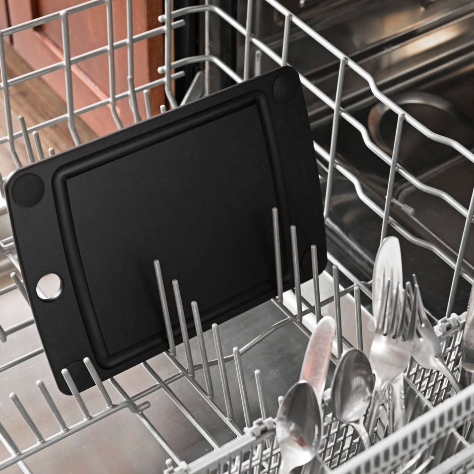 Black Epicurean all-in-one series cutting board inside a dishwasher with silverware around