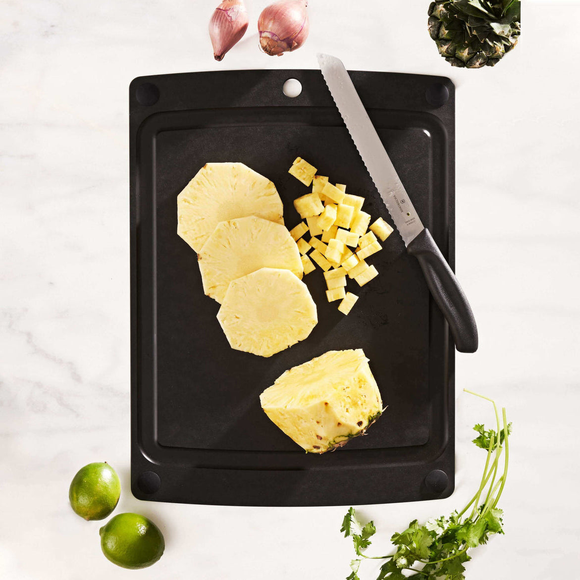 Sliced pineapple on a Epicurean all-in-one series cutting board with a knife and limes on a white background