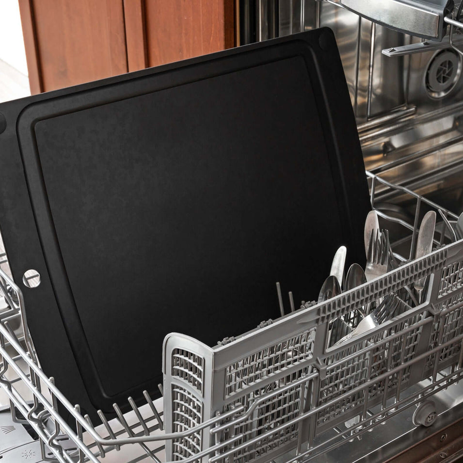 Black Epicurean non-slip all-in-one series cutting board inside an open dishwasher with silverware in the background